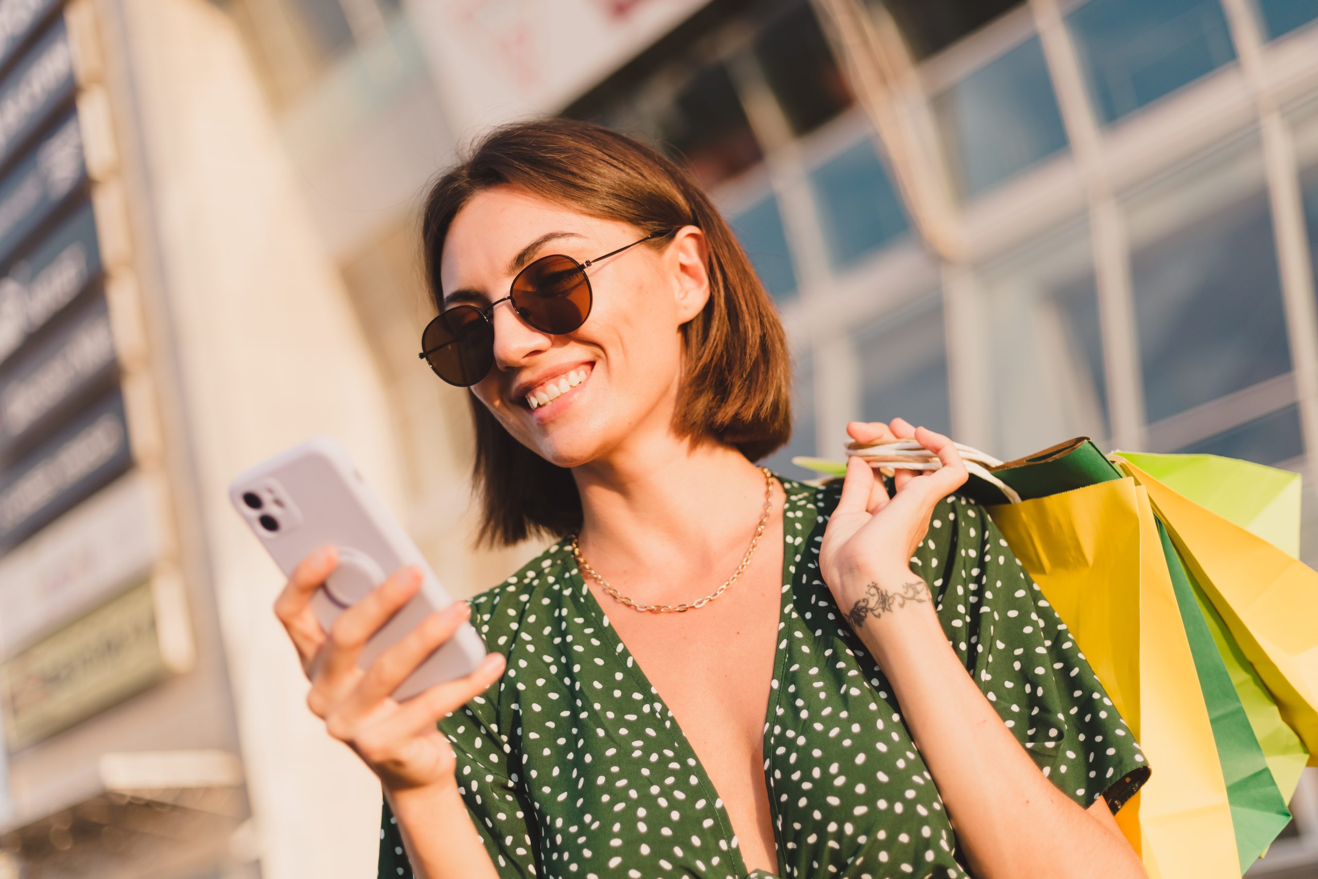 Woman at sunset with colorful shopping bags and parking lot by shopping mall happy with mobile phone Woman at sunset with colorful shopping bags and parking lot by shopping mall happy with mobile phone